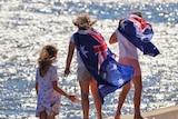 three children draped in Australian flags stand near the water