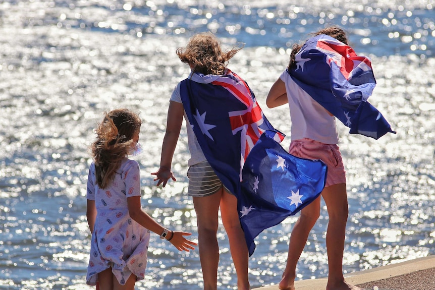 three children draped in Australian flags stand near the water