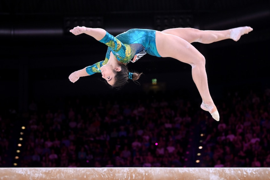 An Australian gymnast twists her body backwards as she is airborne above the balance beam at the Commonwealth Games.