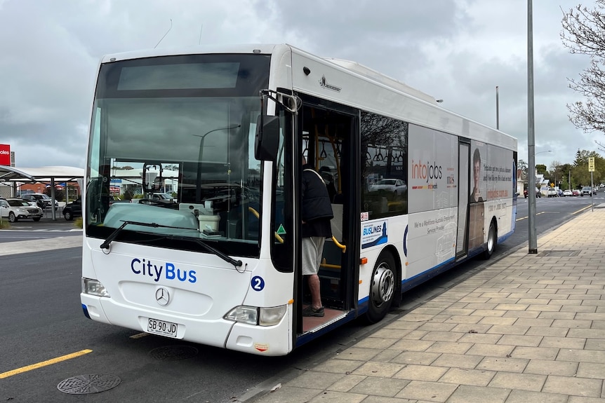 A white bus with the words City Bus on the front next to a paved footpath