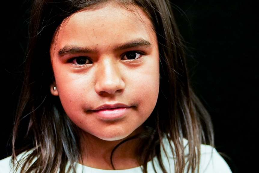 A dark-haired Aboriginal girl, gently smiling at the camera.