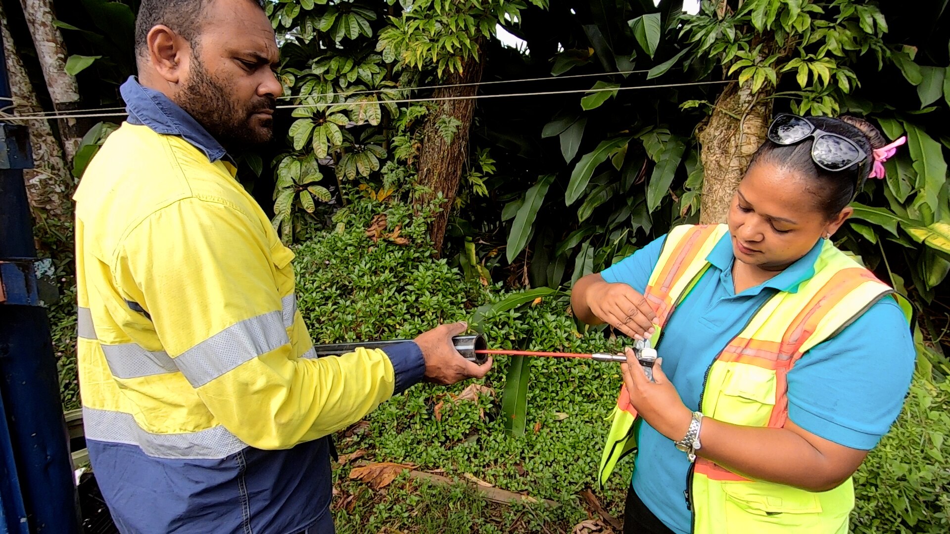 Two people wearing hi-vis vests work together with a long pipe.
