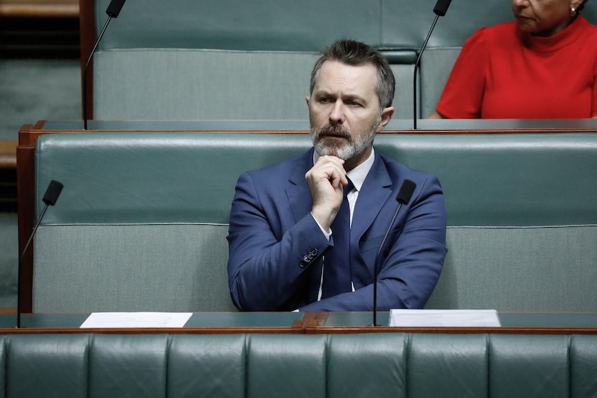 Clare sits in a blue suit, right hand on chin.