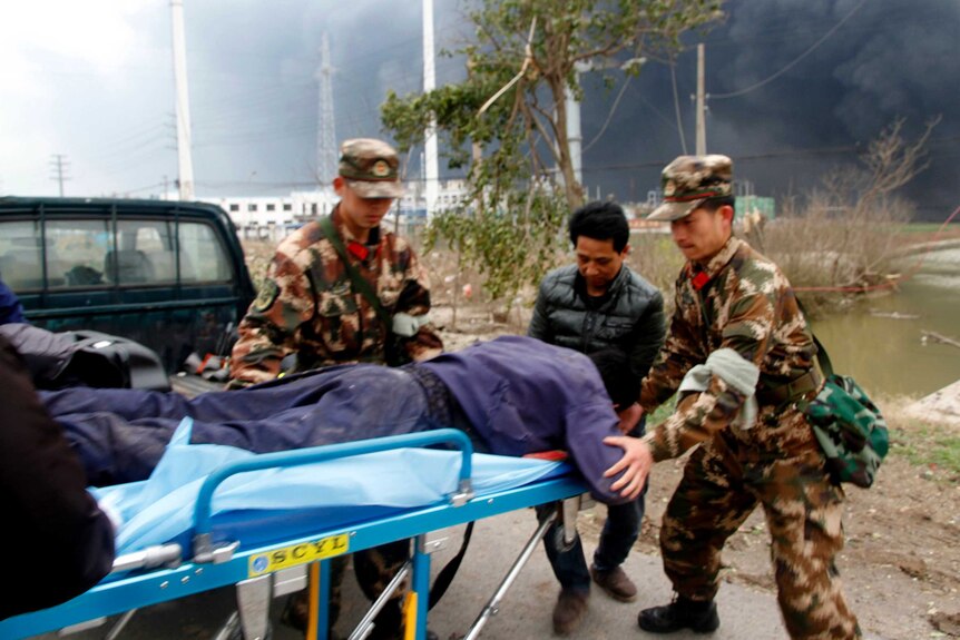 Chinese men in camouflage uniform guide a man face down on a stretcher in a blurry photo with smoke in the background.