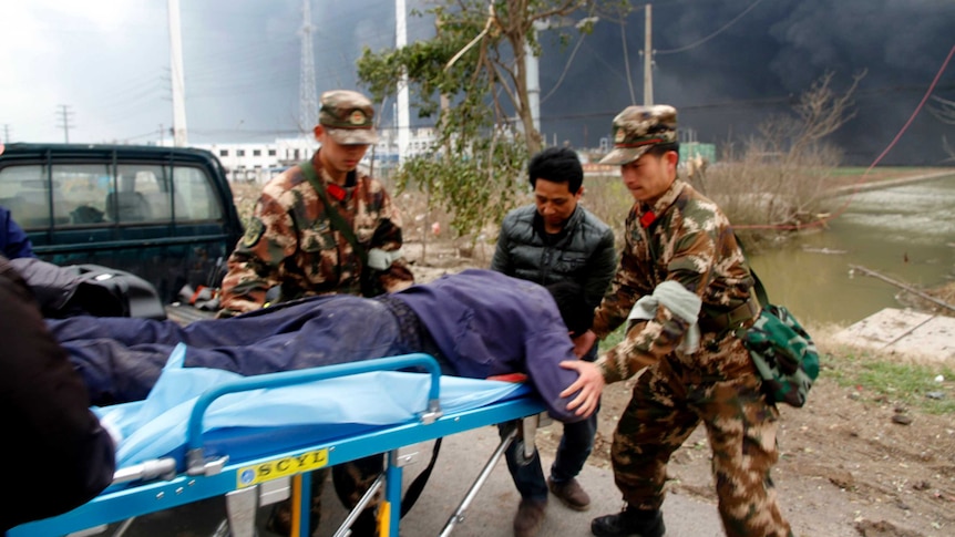 Chinese men in camouflage uniform guide a man face down on a stretcher in a blurry photo with smoke in the background.