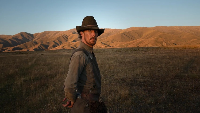 Benedict Cumberbatch standing in front of mountains wearing a hat in the new movie, The Power of the Dog.