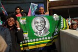 An African National Congress supporter holds a large flag of South African President, Cyril Ramaphosa in green, yellow and black