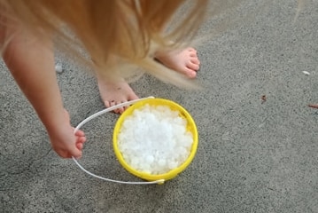 A young girl fills a yellow bucket with hail.