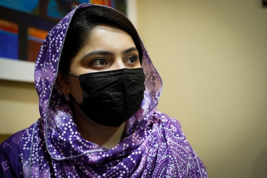 A woman wearing a purple patterned head scarf and black face mask