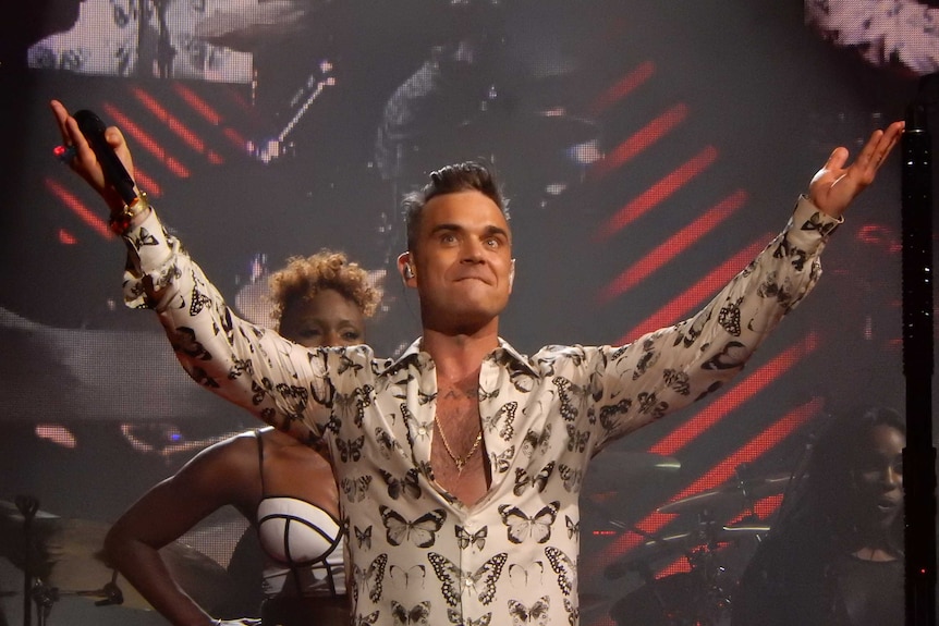 Robbie Williams on stage with his hand up