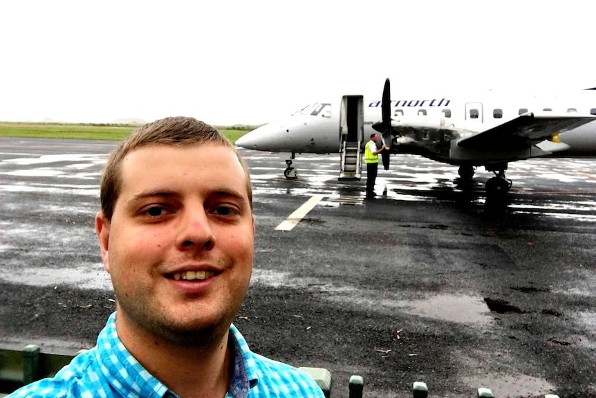 A close profile 'selfie' of a blond-headed, geeky looking man with an old twin-prop aircraft in the bac