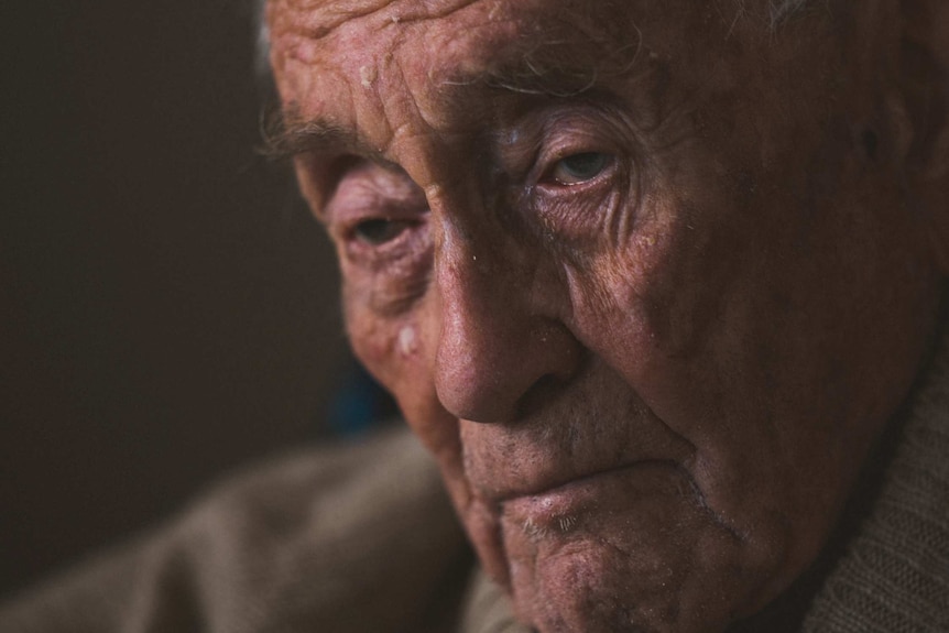 A headshot of a very old man in low light