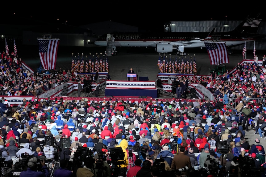 Donald Trump stands on stage in front of a large crowd