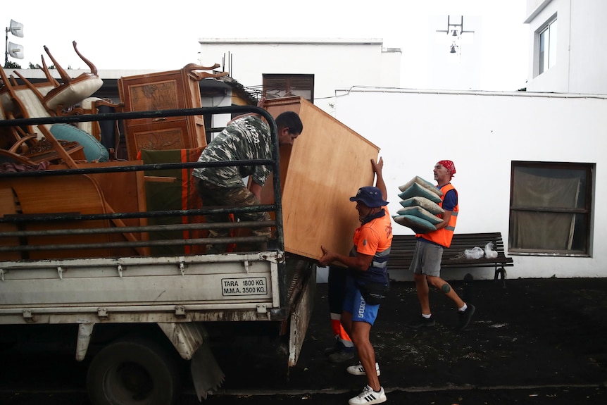 Three men load a large truck with furniture