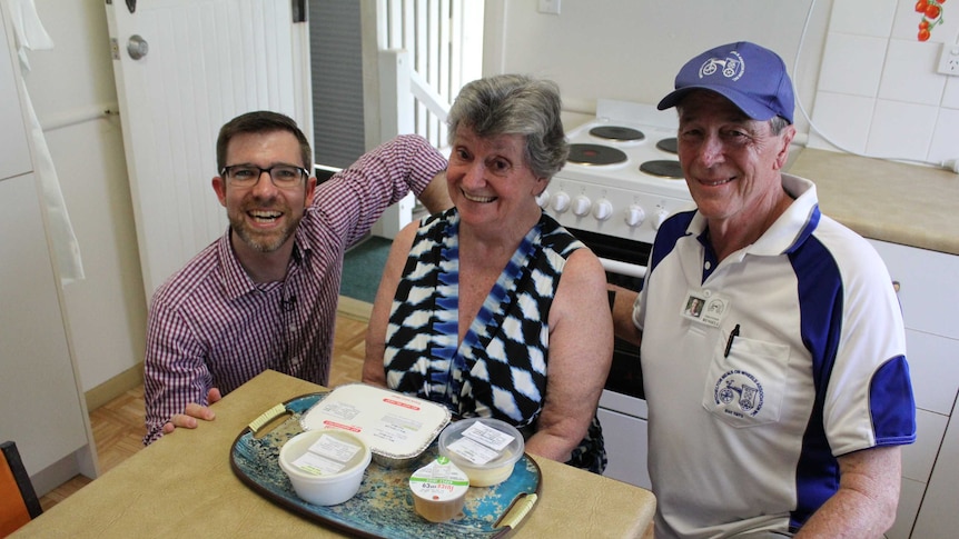 ABC Radio Brisbane presenter Craig Zonca, volunteer Russell Moody and Meals on Wheels client Janice Taylor sitting in a kitchen.