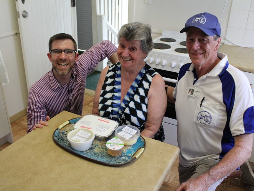 ABC Radio Brisbane presenter Craig Zonca, volunteer Russell Moody and Meals on Wheels client Janice Taylor sitting in a kitchen.