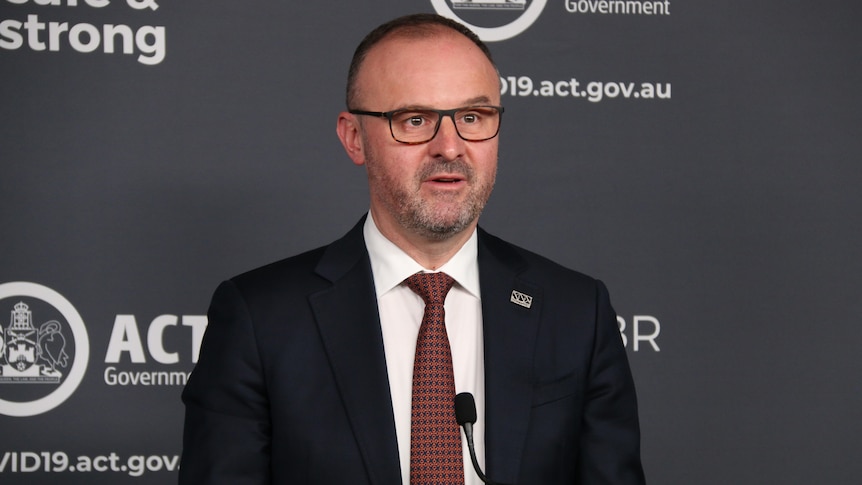 A man wearing glasses and a suit speaks in front of a lectern