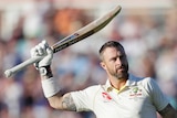 Australia batsman Matthew Wade lifts his bat above his head and holds his helmet in his other hand after reaching a Test century