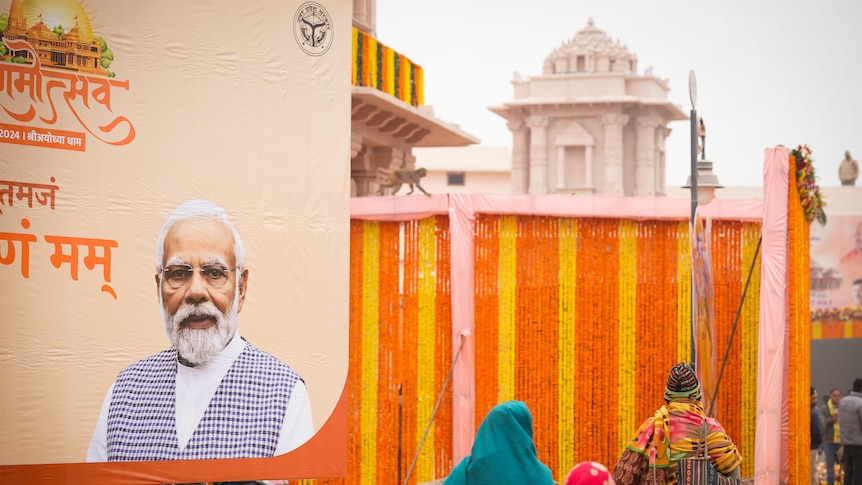 People walk past a billboard with Narendra Modi's face on it, a temple in the background