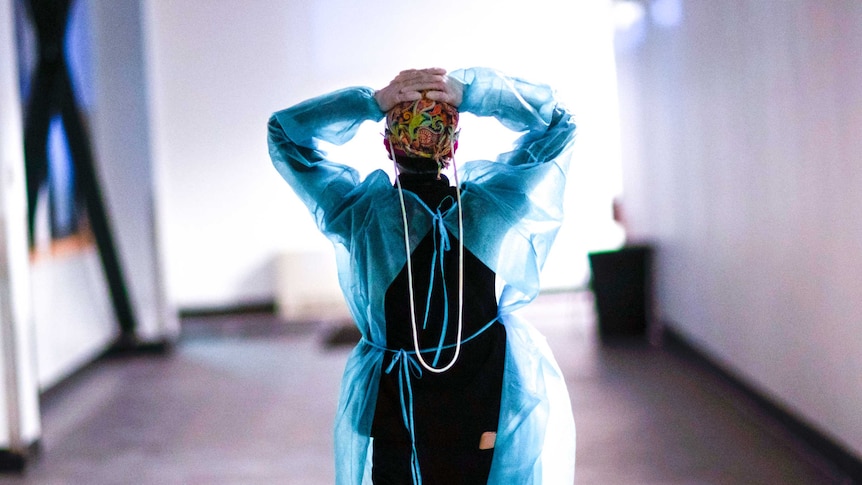 A woman in scrubs walking down a hallway with her hands on her head