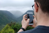 A man holds a phone in front of a natural landscape