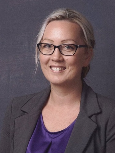 A blonde woman with glasses against a black background.