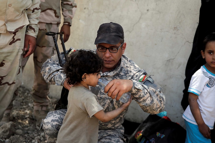A member of the Iraqi Army's 9th Armoured Division gives water to a girl