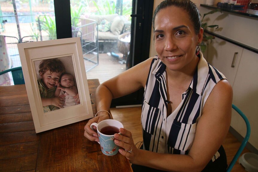 Rebecca Want de Rowe sits at a table with a photo of her two young children.