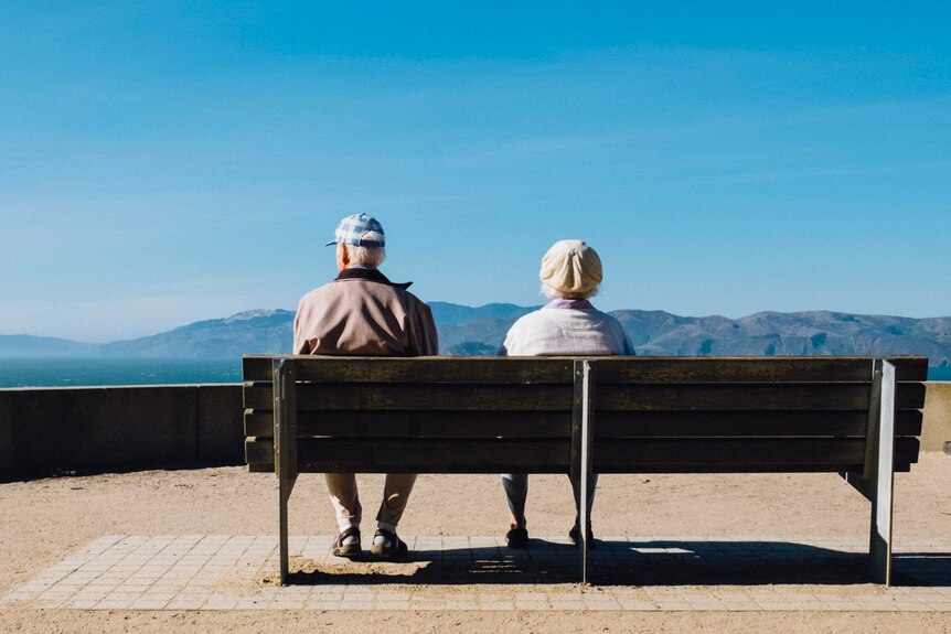 Elderly couple sitting at a bench at the beach.