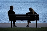 A man and a woman in silhouette sit on a bench at New Farm park in Brisbane.