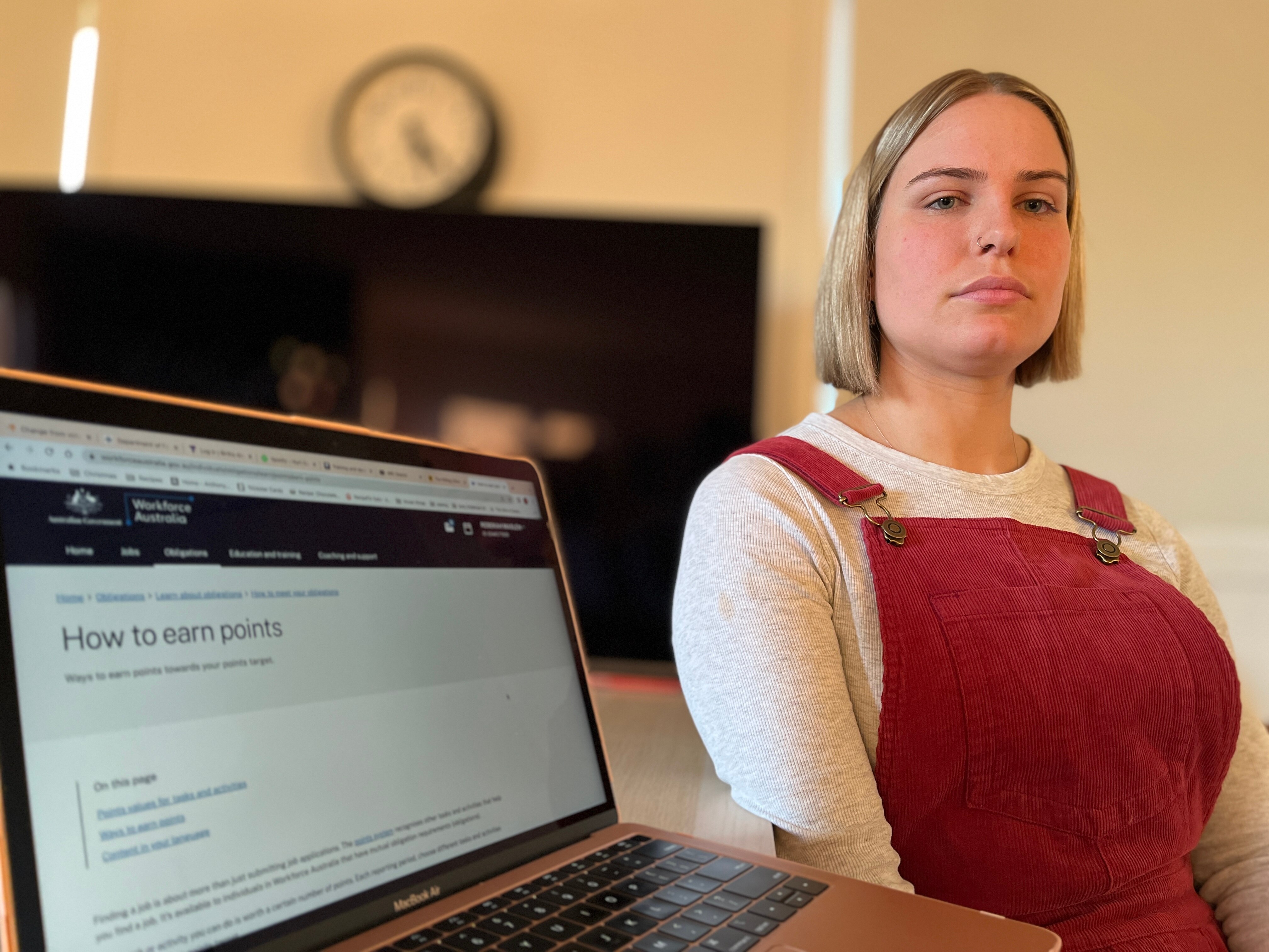 A white woman with blonde hair and red overalls sitting next to a computer screen that says 'how to earn points'
