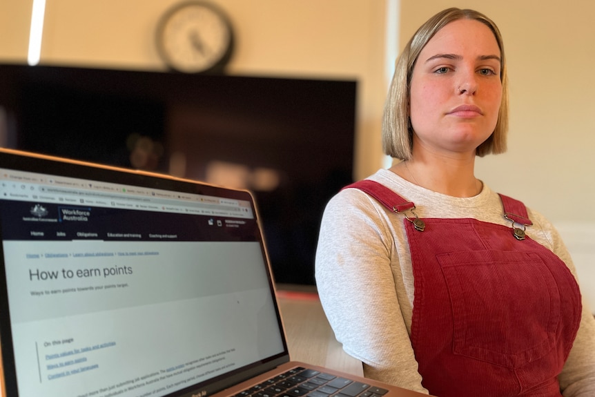 A white woman with blonde hair and red overalls sitting next to a computer screen that says 'how to earn points'