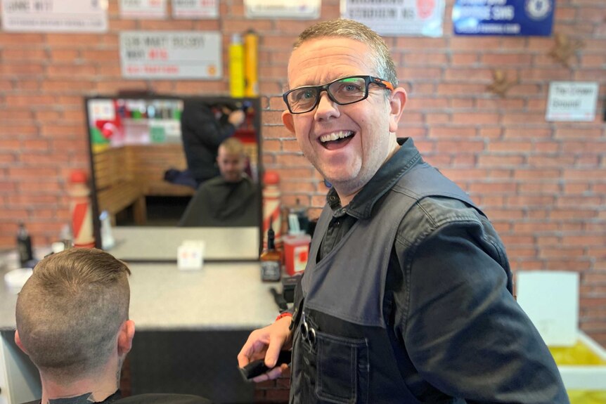 Barber Mark Thompson smiles while cutting a man's hair.