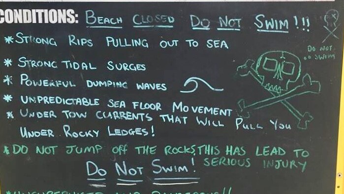 A chalk board sign stands at a beach with information about the conditions there.