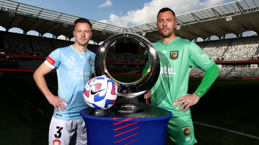 Two rival A-League captains stand behind a pedestal with a ball and the league trophy on it.