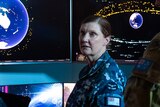 Four soldiers stand inside a dimly lit control room, with screens displaying planet Earth and orbiting satellites.