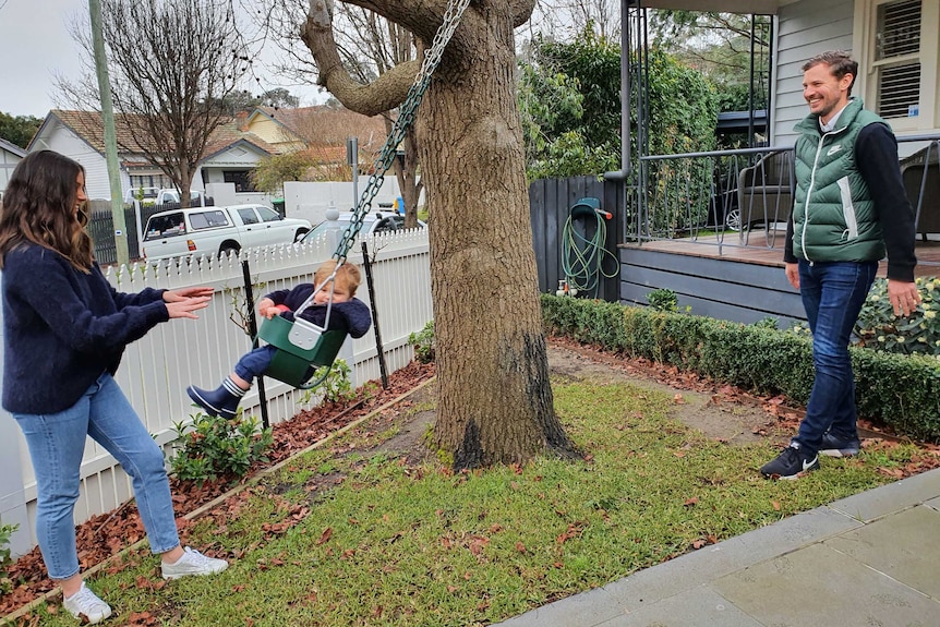 A man and a woman play with their young son on a swing outside their house.