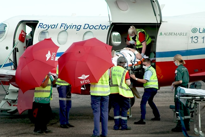 A person on a stretcher is carried out of an RFDS aircraft onto the tarmac