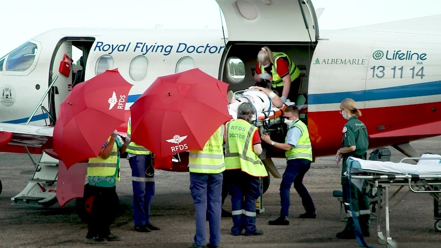 A person off a stretcher is carried off an RFDS plane on the tarmac