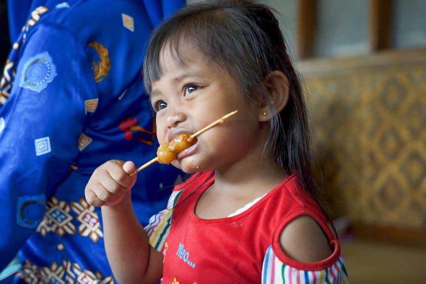 A little girl eating a satay stick