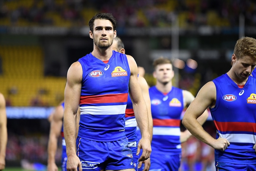 A group of AFL players appear sad as they walk across the field after a loss.