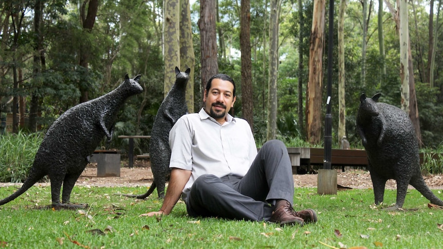 Sina Jamali sits on grass, surrounded by three wallaby statues at the University of Wollongong.