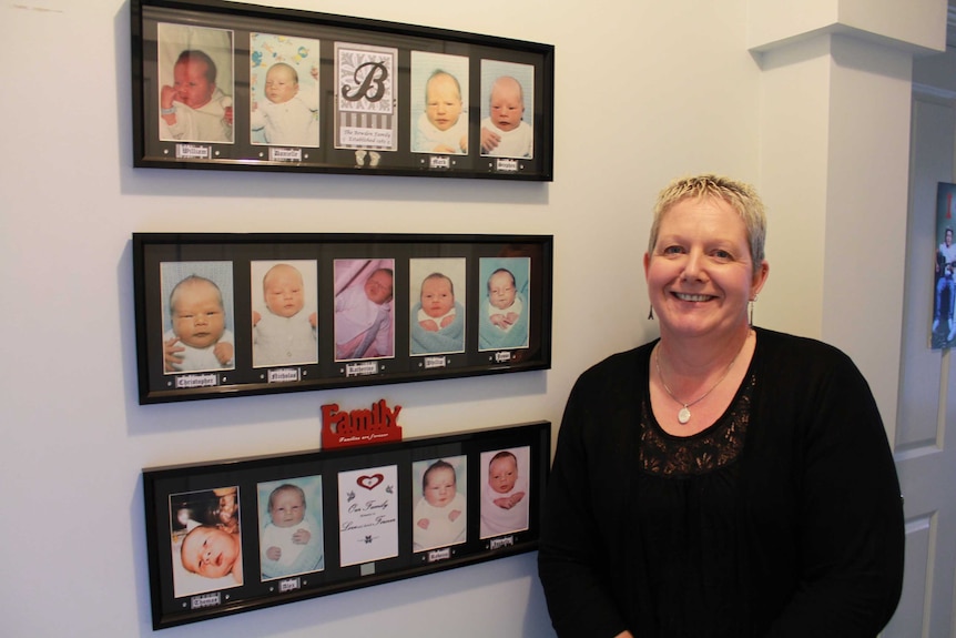 Lyndy Bowden standing next to the baby photographs of her children