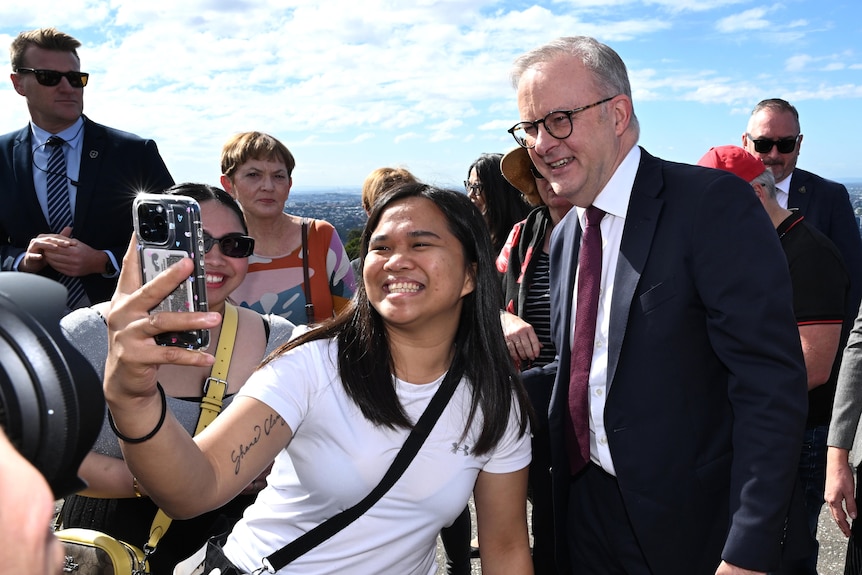 Anthony Albanese smiling as an excited voter, a young woman, takes a selfie with him.