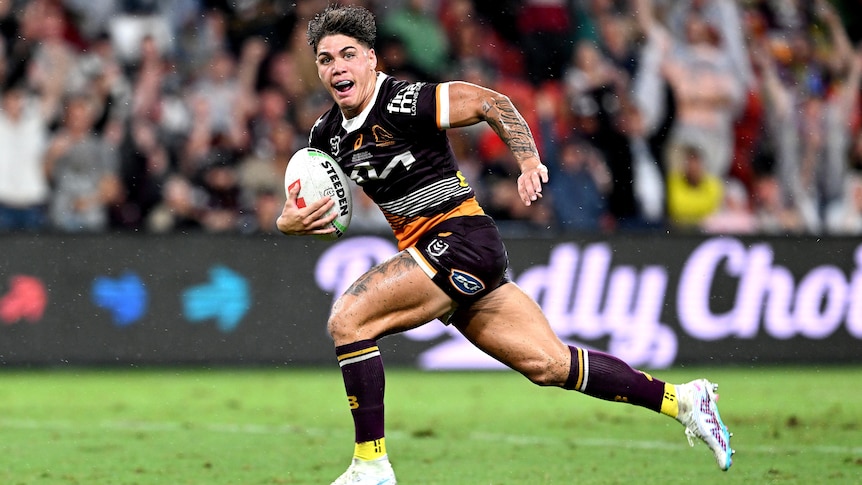 A Brisbane Broncos NRL players looks to his left as he runs away to score a try.