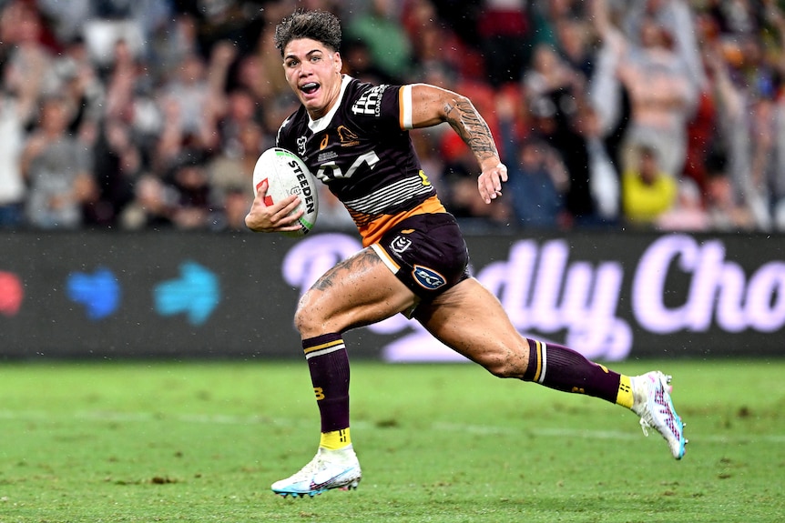 A Brisbane Broncos NRL players looks to his left as he runs away to score a try.