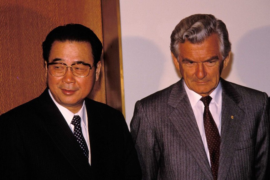 Chinese Premier Li Peng and Bob Hawke stand side by side. Mr Hawke has his eyes downcast and smiles subtly.