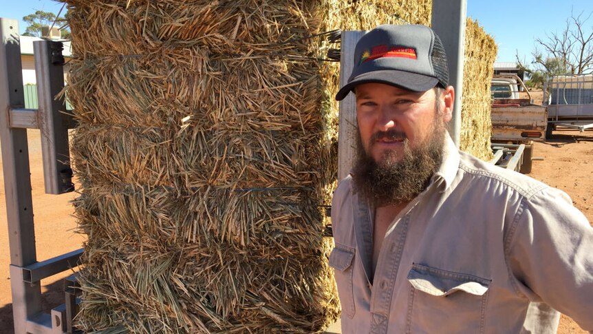 Grazier Nick Andrews standing in front of a trailer of hay and sporting a thick curly beard.