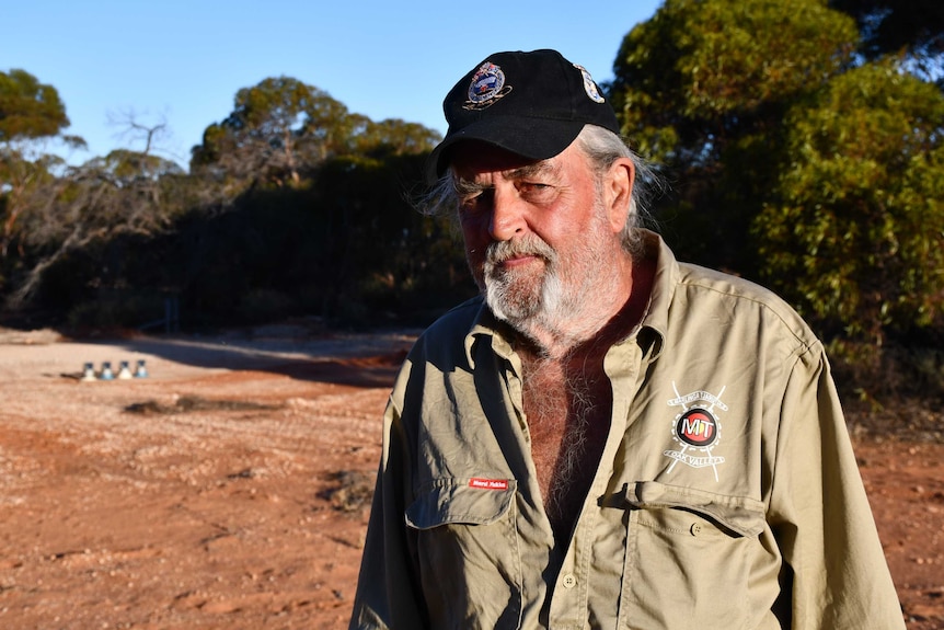 A scruffy man in a black cap and khaki clothes.