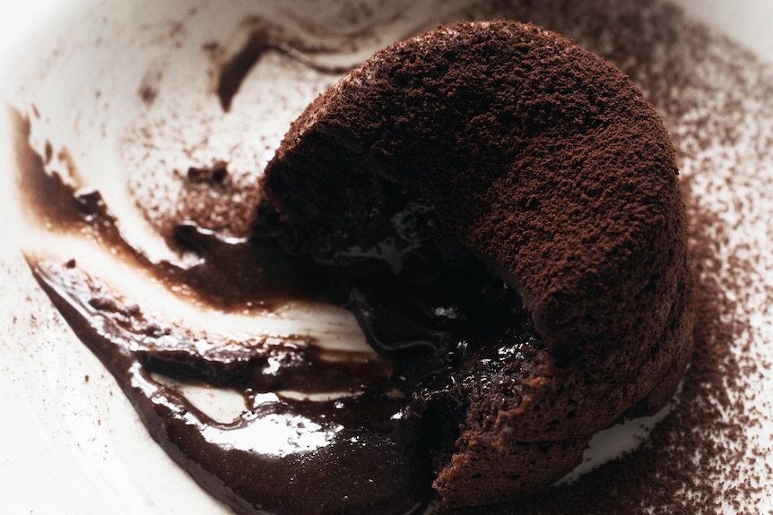 Individual chocolate self-saucing pudding, dusted with cocoa powder, fudgy inside revealed.